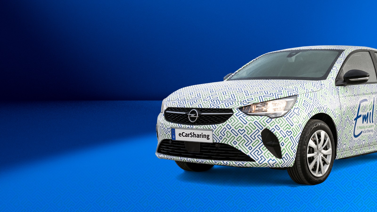 Opel Corsa-e mit Emil eCarSharing-Branding auf blauem Hintergrund ragt rechts bis zu Hälfte ins Bild hinein. 