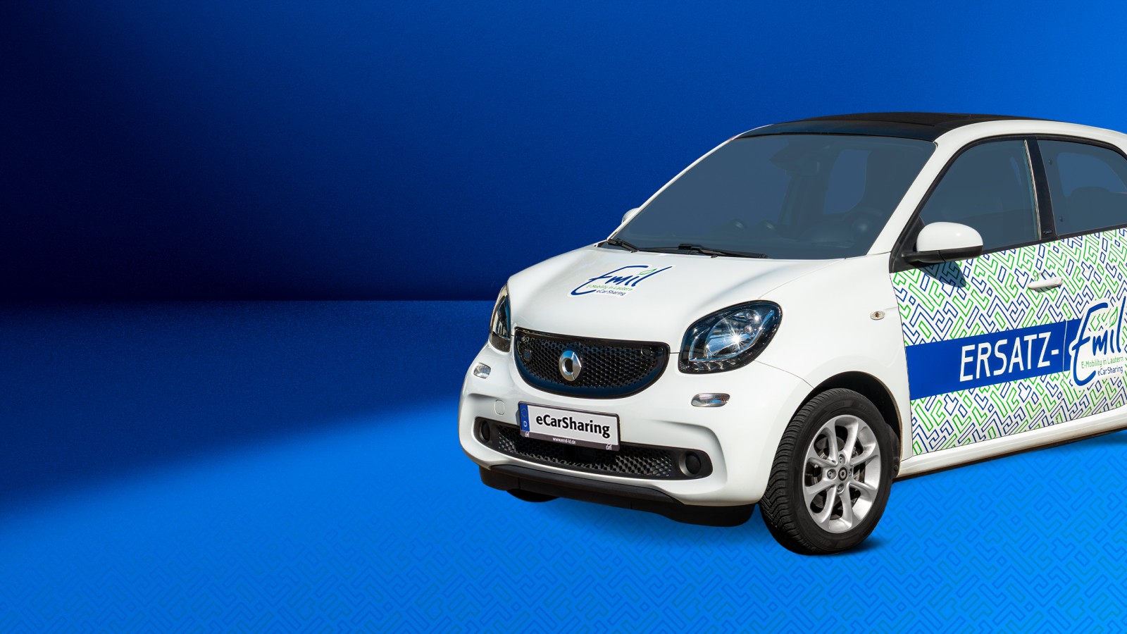 Skoda Enyaq mit Emil eCarSharing-Branding auf blauem Hintergrund ragt rechts bis zu Hälfte ins Bild hinein. 
